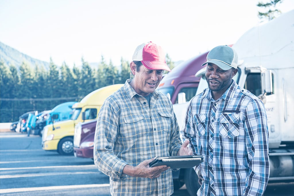 Two truckers looking at a tablet smiling